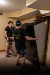 two-men-moving-large-refrigerator-basement Professional crew providing Moving Company in Barrie, ON services for a residential relocation